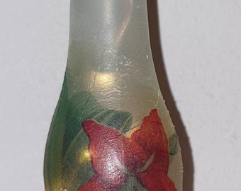 May include: Frosted glass bottle with a black stopper, adorned with a red flower and green leaves design. The bottle is lit with small fairy lights, creating a warm glow. A decorative item.