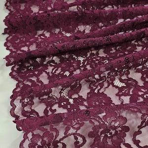 Peut inclure: Gros plan sur un tissu en dentelle bordeaux à motifs floraux. Le tissu délicat est drapé, mettant en valeur le design et la texture complexes. La dentelle a un bord festonné.