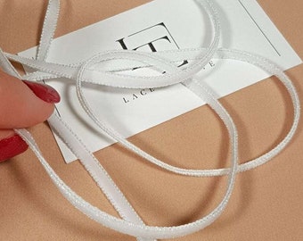 May include: White satin ribbon with a scalloped edge. The ribbon is on a light brown surface and a white card with the text "Lace" is visible.