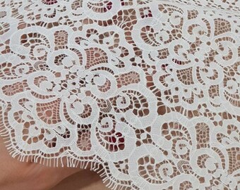 May include: White lace fabric with a delicate floral pattern. The fabric has a scalloped edge and is perfect for crafting or sewing projects.