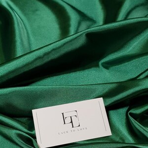 May include: A white card with the text "Lace to Love" and a stylized "LT" logo on a green satin fabric background.