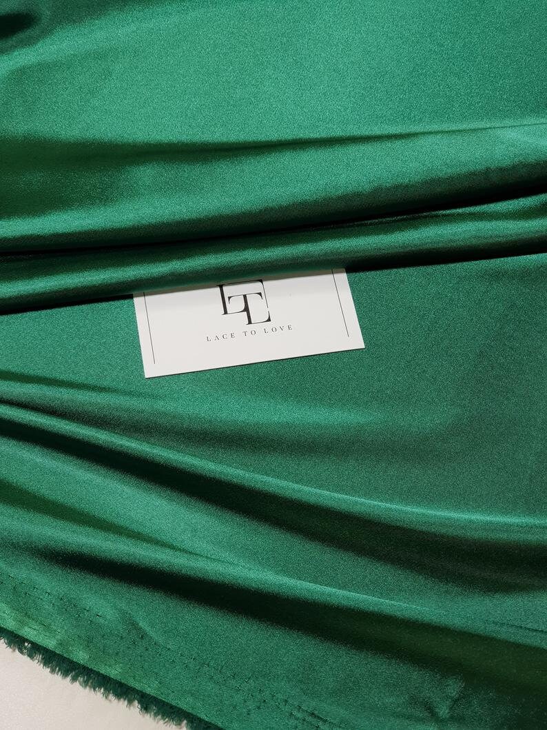 May include: A close-up of a deep green fabric with a subtle sheen. The fabric is folded and draped, showcasing its texture. A white label with the text "Lace To Love" is visible in the center of the image.