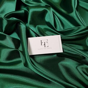 May include: A close-up of a deep green satin fabric with a white card that says "Lace to Love" in black text.
