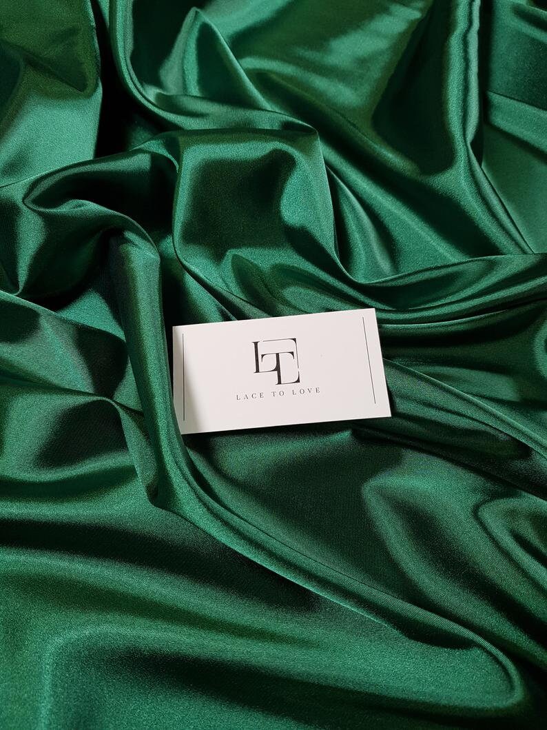 May include: A close-up of a deep green satin fabric with a white card that says "Lace to Love" in black text.