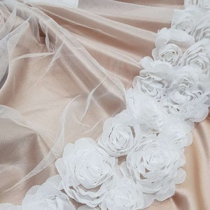 May include: White tulle fabric with a border of white 3D floral appliques. The fabric is sheer and delicate, and the flowers are soft and fluffy.