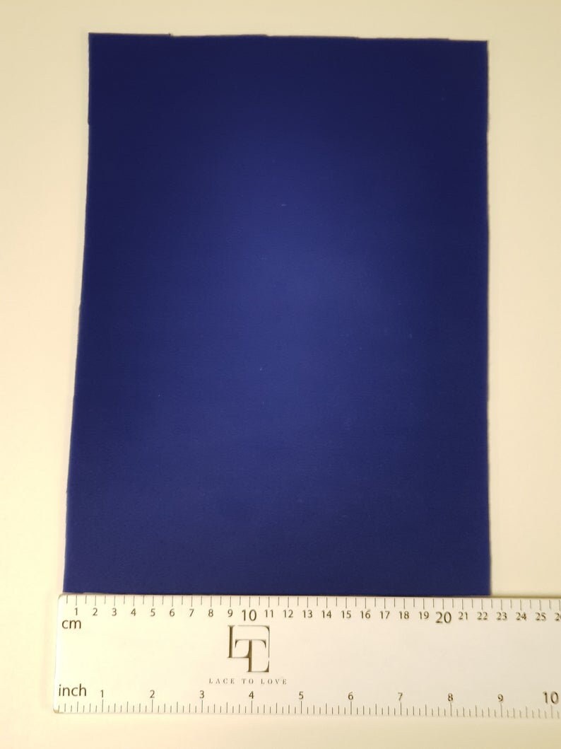 May include: A solid blue piece of fabric measuring 25 cm by 20 cm. The fabric is laid flat on a white surface with a ruler underneath.