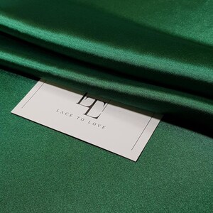 May include: A white card with the text "Lace to Love" and the letter "L" in a larger font size, sitting on a green satin fabric.