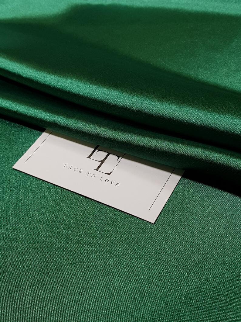 May include: A white card with the text "Lace to Love" and the letter "L" in a larger font size, sitting on a green satin fabric.