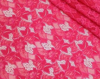 May include: Pink lace fabric with a floral pattern. The lace has a delicate, intricate design with small white dots.