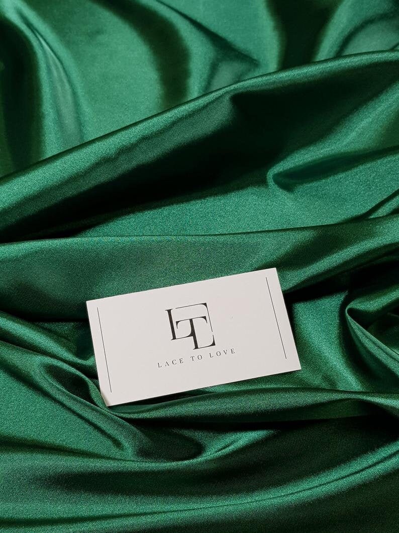 May include: A white card with the text "Lace to Love" and a stylized "LT" logo on a green satin fabric background.