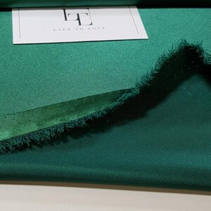 May include: A close-up of a folded piece of emerald green fabric with a frayed edge. The fabric is smooth and has a slight sheen. A white card with the text "Lace to Love" is visible in the background.