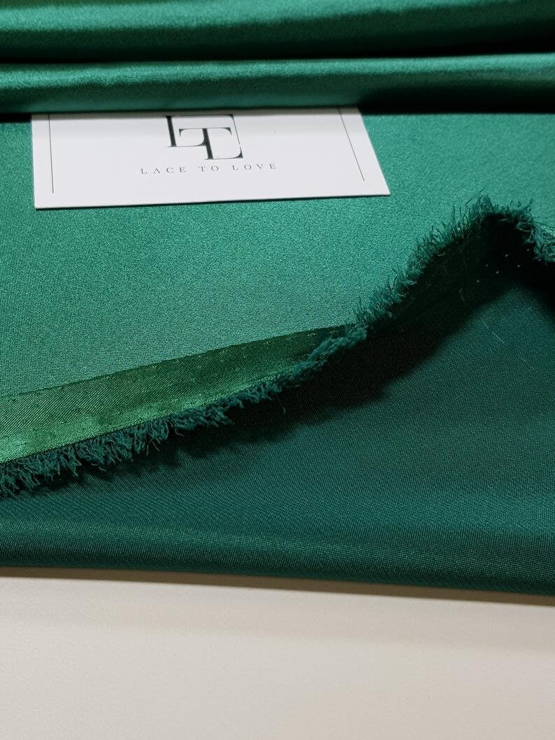 May include: A close-up of a folded piece of emerald green fabric with a frayed edge. The fabric is smooth and has a slight sheen. A white card with the text "Lace to Love" is visible in the background.