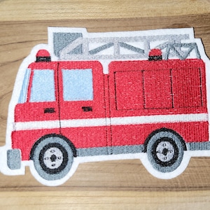 Könnte beinhalten: Rotes und weißes gesticktes Feuerwehrwagen-Patch mit einer Leiter oben. Der Wagen hat einen weißen Streifen am unteren Rand und schwarze Räder.