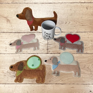 Könnte beinhalten: Eine Sammlung von Dackel-Artikeln. Enthält einen Plüschdackel, eine weiße Tasse mit dem Text "I'm a Dog Lover" und bestickte Dackel-Untersetzer mit Herz- und Kreisakzenten. Die Artikel sind braun, rosa, rot und grün.