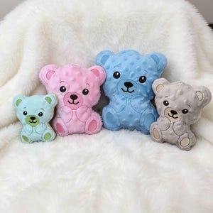 以下が含まれることがあります： ドット柄のテクスチャ生地で作られた4つのクマのぬいぐるみ。一番小さいのはライトグリーンで、中くらいのピンクのクマ、大きな青いクマ、中くらいの灰色のクマが続きます。それぞれのクマには、刺繍された顔のディテールと足のパッドが付いています。