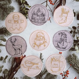 May include: A collection of embroidered Christmas coasters with various festive designs. The coasters feature images of a gingerbread man, a snow globe, a stocking, Santa Claus, a reindeer, a snowman, a bird, and a mug with "Merry Christmas" text.