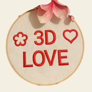 May include: A white embroidery hoop with red embroidery that reads "* 3D LOVE" with a flower and heart design.