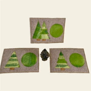 Könnte beinhalten: Drei Filzuntersetzer mit einem grünen und weißen Weihnachtsbaumdesign und einem grünen Kreis. Die Untersetzer befinden sich auf einer hellbraunen Oberfläche.