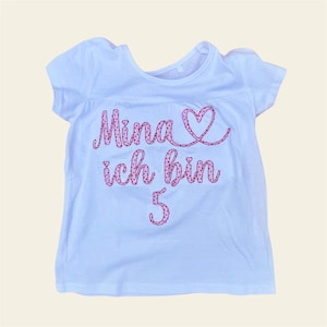 Könnte beinhalten: Weißes T-Shirt mit rosa gesticktem Text, der "Mina ich bin 5" mit einem rosa Herz sagt.