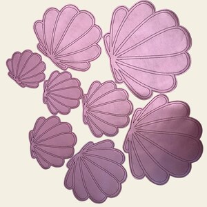 Puede incluir: Un conjunto de ocho conchas de fieltro rosa de diferentes tamaños. Las conchas son todas en forma de concha de vieira con un diseño texturizado en relieve.