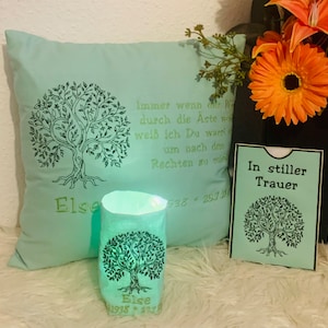 May include: A green cushion with a tree design and the text "Immer wenn der Wind durch die Aste weht, weiß ich Du warst um nach dem Rechten zu suchen" and "Else 1938 - 25.7.2020". A green candle with a tree design and the text "Else 1938 - 2020". A green card with a tree design and the text "In stiller Trauer".