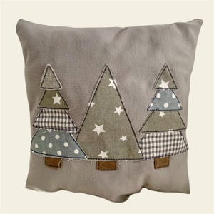 Può includere: Un cuscino grigio con tre alberi di Natale applicati. Gli alberi sono realizzati con tessuti diversi con stelle bianche, gingham e pois.