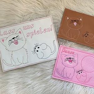 May include: Three decorative felt cat and mouse designs. One is white with the text "Lass uns spielen!" and a pink border. Another is brown, and the third is pink with the text "Lasse". All feature embroidered cat and mouse illustrations.