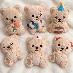 Puede incluir: Seis adornos de peluche beige con forma de oso con detalles bordados. Uno sostiene una flor rosa, uno lleva una mochila azul con un libro ABC, uno usa un gorro de fiesta azul con un pastel, uno es sencillo, uno usa una cofia de enfermera y uno tiene lazos rosas.