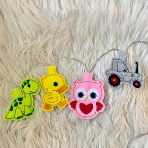 May include: A string of fairy lights with felt animal and vehicle cutouts. The cutouts include a green dinosaur, a yellow duck, a pink owl, and a gray tractor.