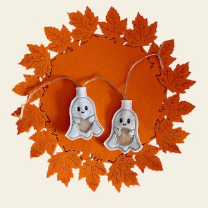 May include: A string of lights with white felt ghost ornaments holding hearts. The lights are on a orange felt background with a circle of orange felt maple leaves around the edge.