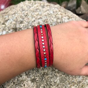 Könnte beinhalten: Ein rotes Lederarmband mit geflochtenem Design und silbernen und türkisfarbenen Akzenten.