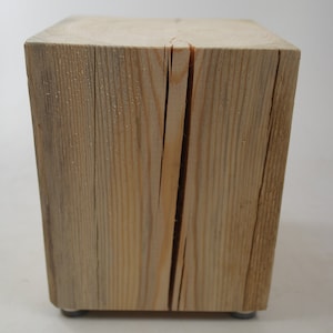 Könnte beinhalten: Ein natürlicher Holzblock mit rauer, rustikaler Textur. Der Block ist hellbraun und quadratisch. Er hat einen Riss in der Mitte und steht auf einer weißen Oberfläche.