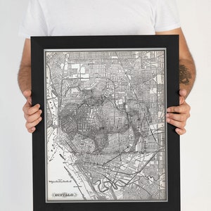 May include: A black framed vintage map of Buffalo, New York. The map is in black and white and shows the city's streets and landmarks. The map is framed in a black frame with a silver mat.