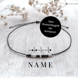 Könnte beinhalten: Ein schwarzes Armband aus Schnur mit weißen und schwarzen Perlen, die "NAME" in einer einfachen Schriftart buchstabieren. Das Armband ist mit einem Knoten gebunden und hat an jedem Ende eine silberne Perle. Der Text "Dein Wunschbegriff als Armband" ist im Bild sichtbar.