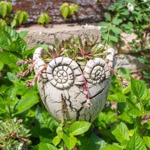 Può includere: Un set di tre tazze in ceramica con smalto screziato color crema. Ogni tazza presenta un design dipinto a mano diverso: una foglia blu e verde, un fiore giallo e una bacca rossa. Le tazze hanno un design semplice e moderno.
