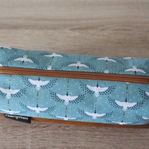 May include: A blue and white zippered pouch with a pattern of white cranes flying against a blue background. The pouch has a brown leather bottom and a red zipper pull.