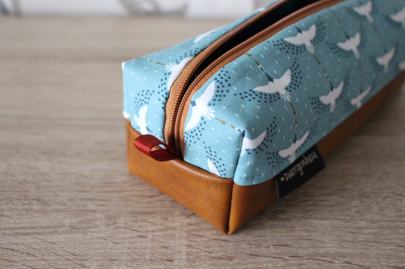 May include: A blue and brown zippered pencil case with a white crane pattern and the text "sweetpepperhouse".
