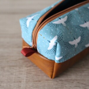 May include: A blue and brown zippered pencil case with a white bird pattern. The case has a red zipper pull.