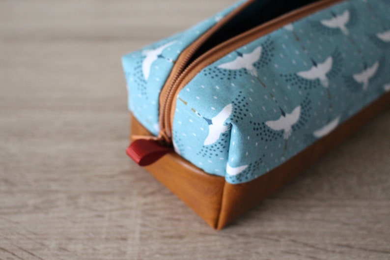 May include: A blue and brown zippered pencil case with a white bird pattern. The case has a red zipper pull.