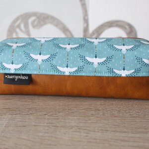 May include: A brown leather pencil case with a blue fabric top featuring a white crane pattern. The fabric has a gold and blue dot pattern. The case has a small label that says "zwergenhexe".
