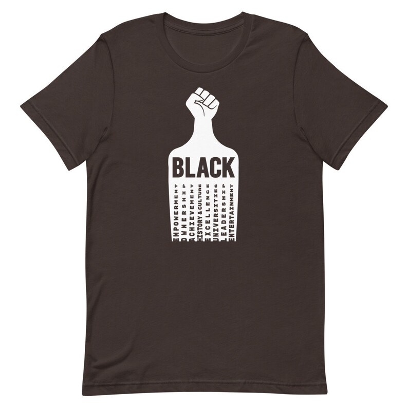 K&ouml;nnte beinhalten: Ein dunkelbraunes T-Shirt mit einer wei&szlig;en Faust, die in die Luft erhoben ist. Die Faust h&auml;lt ein wei&szlig;es Rechteck mit dem Wort "BLACK" in Gro&szlig;buchstaben. Das Rechteck ist mit W&ouml;rtern in Gro&szlig;buchstaben gef&uuml;llt, darunter "EMPOWERMENT", "OWNERSHIP", "ACHIEVEMENT", "HISTORY & CULTURE", "DIVERSITY", "UNIVERSITIES", "EXCELLENCE", "LEADERSHIP", "ENTERTAINMENT".