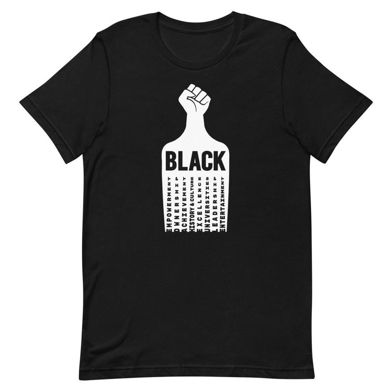 K&ouml;nnte beinhalten: Schwarzes T-Shirt mit einem erhobenen Faust-Motiv und dem Wort "BLACK" in wei&szlig;en Buchstaben. Das Wort "BLACK" ist umgeben von W&ouml;rtern, die die schwarze Erfahrung beschreiben, darunter "Empowerment", "Ownership", "Achievement", "History & Culture", "Excellence", "Universities", "Leaders" und "Entertainment".