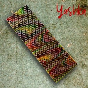 Może przedstawiać: Prostokątny przedmiot z wzorem plastra miodu w odcieniach zieleni, żółci, czerwieni i fioletu. Słowo "Yashka" jest napisane czerwoną czcionką w prawym górnym rogu. Przedmiot znajduje się na teksturowanej, szaro-zielonej powierzchni.