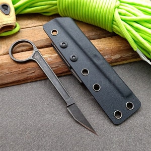 Puede incluir: Una funda de cuchillo de cuero negro con cierre de presi&oacute;n met&aacute;lico y un cuchillo de metal negro con mango redondeado.