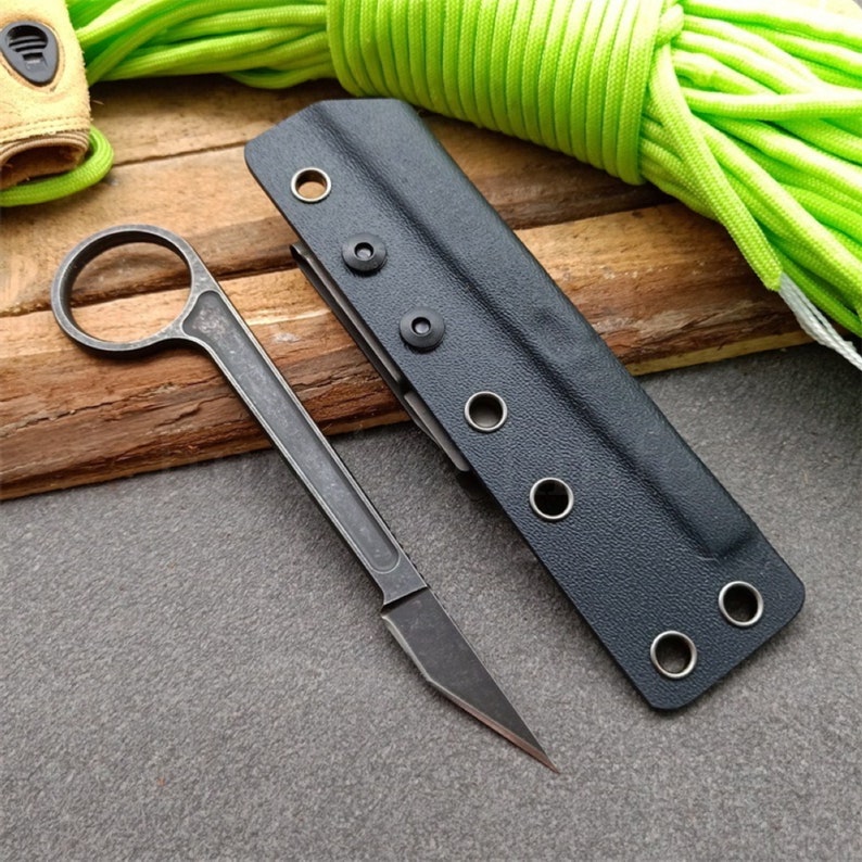 Puede incluir: Una funda de cuchillo de cuero negro con cierre de presi&oacute;n met&aacute;lico y un cuchillo de metal negro con mango redondeado.