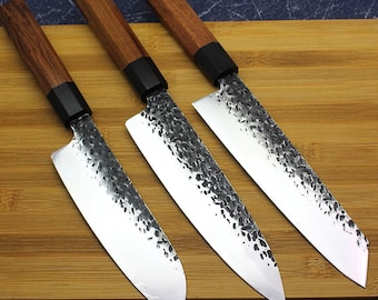 May include: Three Japanese-style kitchen knives with wooden handles and black accents. The blades are made of stainless steel and have a hammered finish.