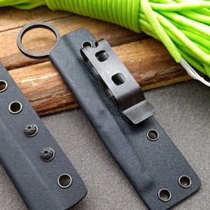 Puede incluir: Dos fundas de cuchillo de cuero negro con broches met&aacute;licos y un clip met&aacute;lico. Una funda tiene un anillo met&aacute;lico.