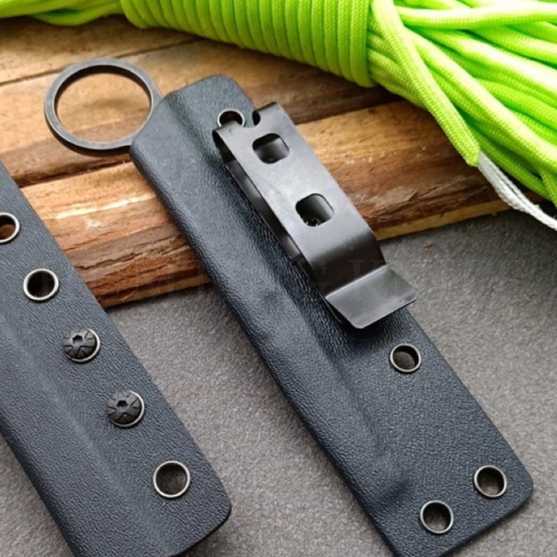 Puede incluir: Dos fundas de cuchillo de cuero negro con broches met&aacute;licos y un clip met&aacute;lico. Una funda tiene un anillo met&aacute;lico.