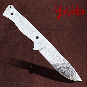 Puede incluir: Una hoja de cuchillo de plata con una hoja estampada y un mango con dos agujeros. La hoja está sobre una superficie marrón.