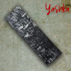 May include: A rectangular item with a black and grey pattern. The word "Yashka" is written in red script in the upper right corner. The item is set against a mottled, olive-green background.